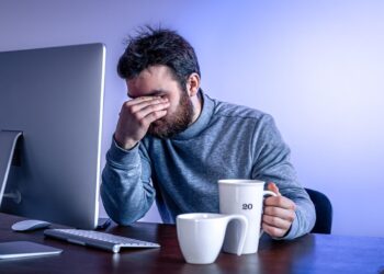 Homem frustrado segurando uma xícara de café enquanto usa um computador com Windows lento.