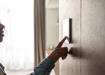 Pessoa tocando um interruptor inteligente em uma parede. Imagem representando tecnologia de automação residencial