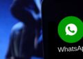 Logo do WhatsApp em primeiro plano com uma silhueta de uma pessoa ao fundo, representando possíveis ameaças de golpes online.